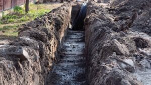 A freshly dug trench with soil piles, showing pipes and ready for the backfilling process.