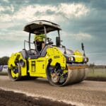 A yellow road roller ensures ideal soil compaction on a dirt road under a cloudy sky.