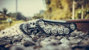 Small tracked robot aids automation in construction on rocky terrain with greenery behind.