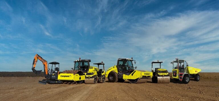 A lineup of construction vehicles on a dirt road under a blue sky with scattered clouds showcases the challenges of Australian construction. The vehicles, including an excavator, road rollers, and a cement mixer, are positioned side by side on the open landscape.