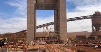 Mining Ops - Conplant Pty Ltd - Conplant Pty Ltd Industrial construction site with a tall concrete arch, cranes and conveyor belts, orange safety barriers, and workers in hi-vis gear.