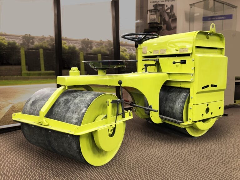 A small, bright yellow road roller displayed indoors on a brown carpeted floor.