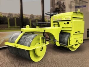 Bright yellow steamroller displayed indoors with Vibratory Compactors on a carpeted floor.