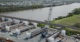 Oscillation - Conplant Pty Ltd - Conplant Pty Ltd Construction site along a river with an elevated bridge overhead, a tall crane, and rows of concrete foundations and equipment.
