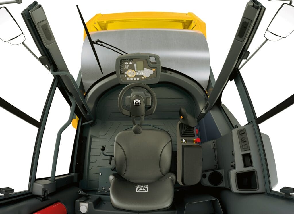 Interior view of the RC-2 series construction vehicle cabin featuring a steering wheel, modern digital control display, ergonomic seat, and various controls. The cabin boasts large windows and a yellow roof, ensuring a clear view of the surroundings.