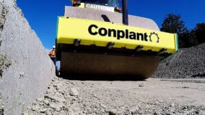Remote Unammned 3 - Conplant Pty Ltd Unmanned Roller steamroller flattening gravel with "Conplant" sign, viewed from ground level.