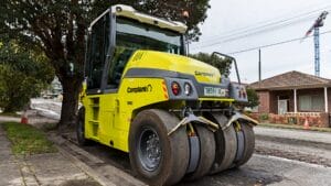 Yellow road roller parked on a street, aiding resilient roads and road construction near houses.