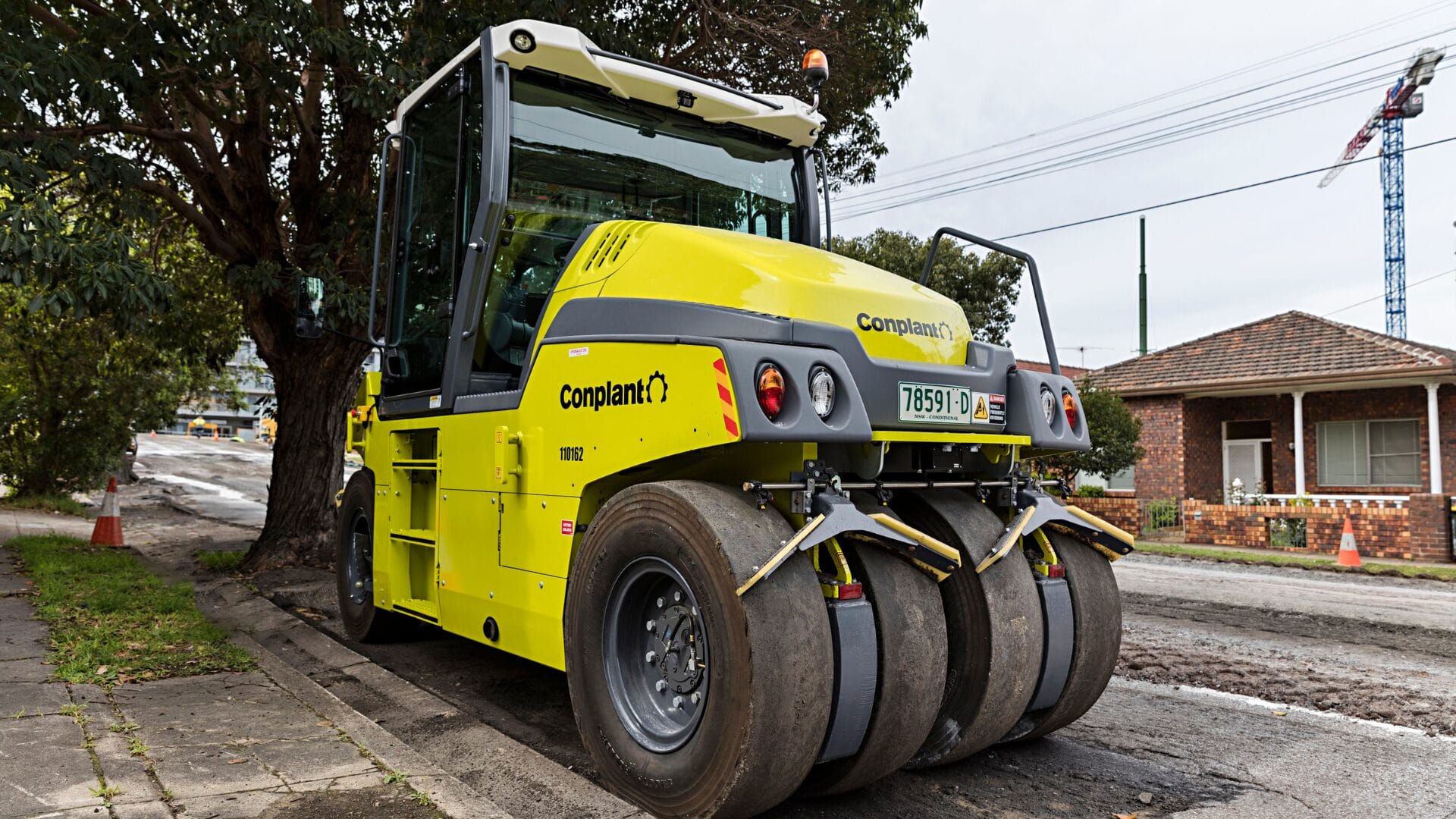 Yellow road roller parked on a street, aiding resilient roads and road construction near houses.