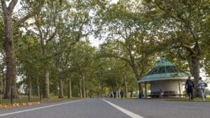 Wide path beneath urban canopy, with people walking and a shelter on the right.