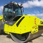 A bright yellow road roller with the "Conplant" logo and "Wacker Neuson" label on its side is parked on a paved area under a clear blue sky. The machine, an impressive example among soil compactors, has large tires and a massive front roller designed for compacting surfaces.