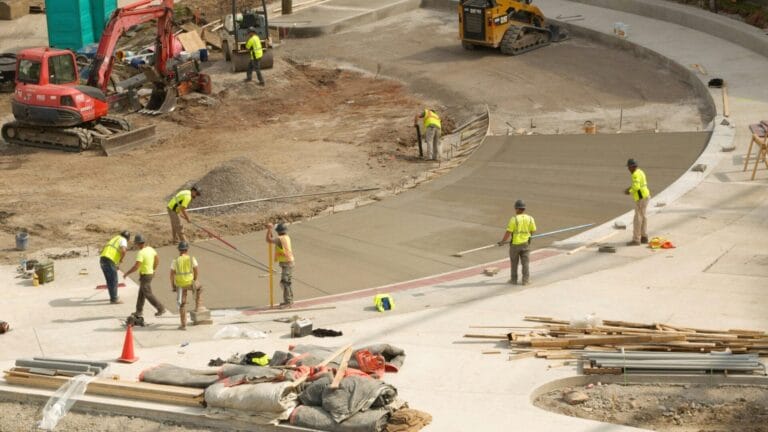 Workers in yellow vests smooth fresh concrete, showcasing civil construction trends for 2026.