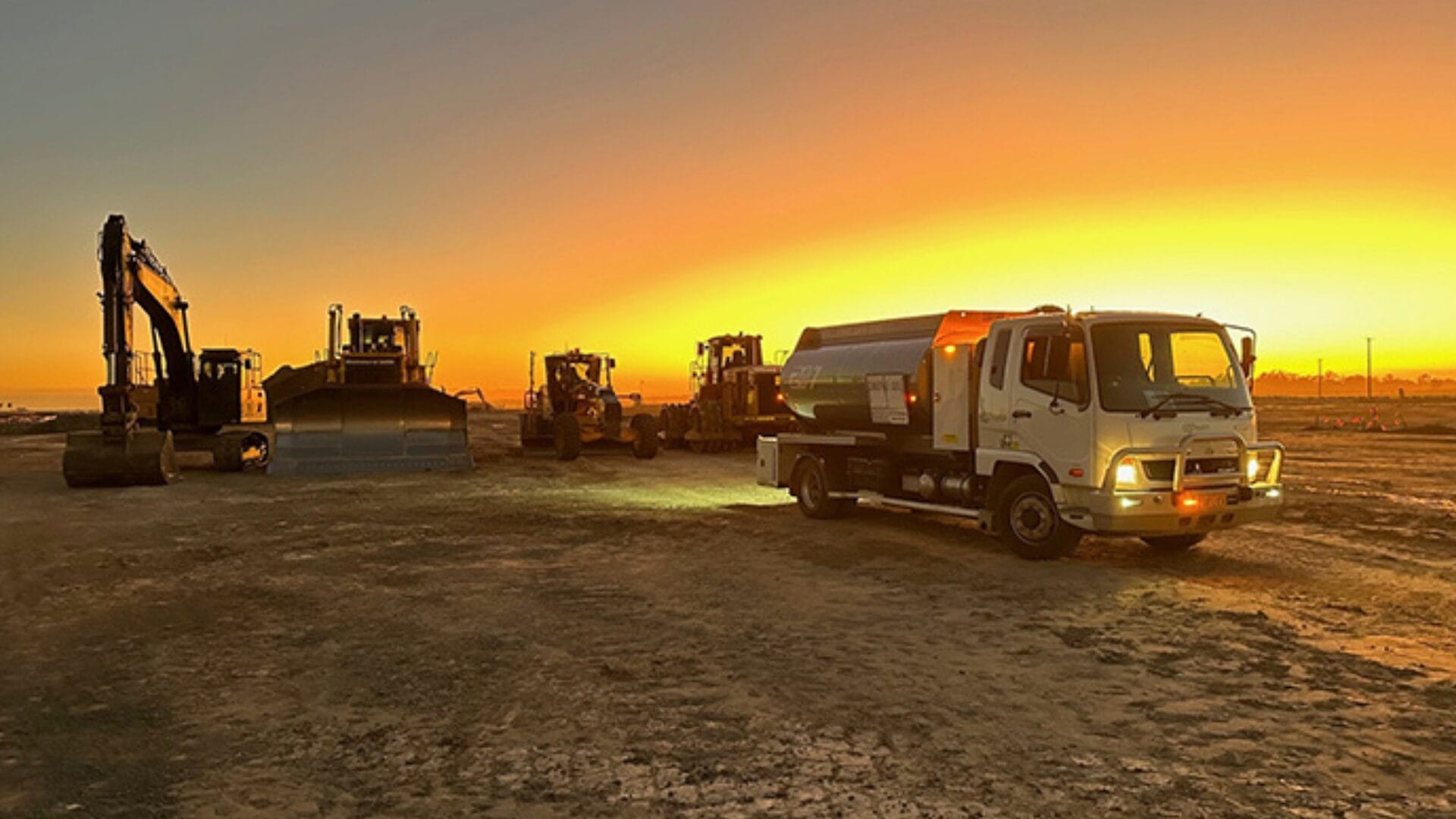 Construction vehicles parked on a dirt site at sunset, highlighting fleet efficiency at work.