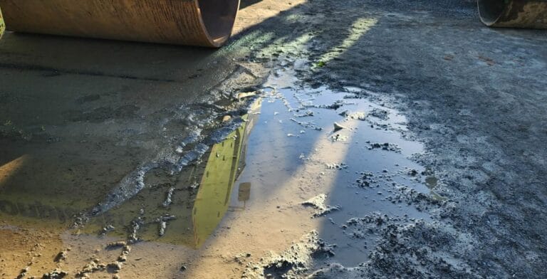 Puddle reflecting construction equipment on muddy ground after wet weather compaction.